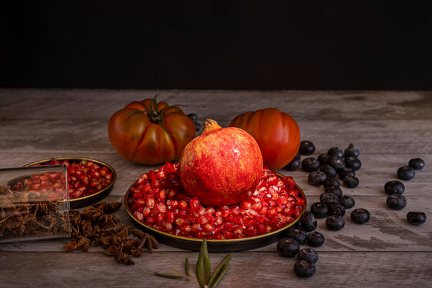 Stillleben mit Granatäpfeln, Körnern, Blaubeeren, Sternanis und rosa Tomaten auf Holztisch - Foto, Bild