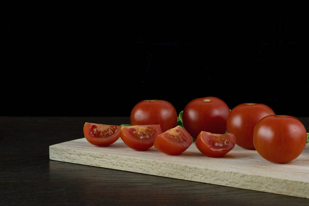 A close-up shot of red tomatoes on a wooden table isolated on dark background. - Photo, image
