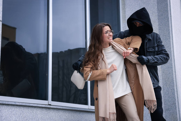 Woman fighting with thief while he trying to steal her bag near building, space for text. Self defense concept - Foto, immagini