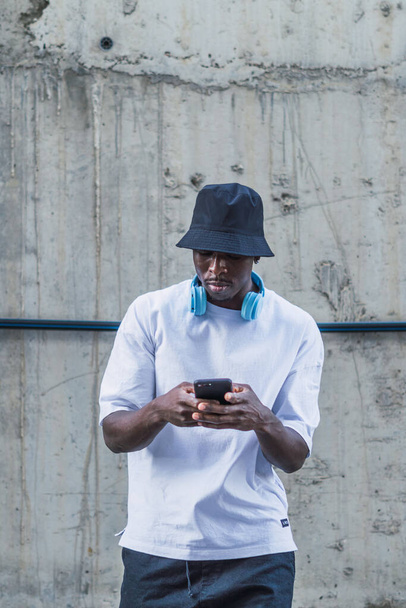 A shot of a man with white t shirt and a blue headset standing in the street and using phone, Spain - 写真・画像
