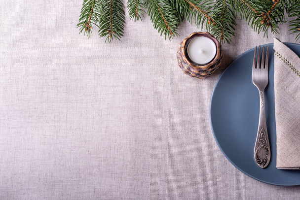 Natural spruce coniferous green branches with white candle in candlesticks in the form of cones, fork and grey linen napkin on grey tableclothe background.  - 写真・画像