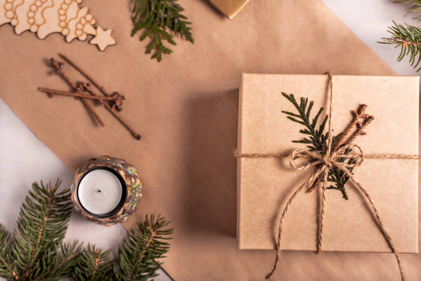 Packing a gift for Christmas and new year in eco-friendly materials: kraft paper, live fir branches, cone, twine, tied with a bow. Tags with mock up, natural decor, hand made, flatlay. Festive mood - Фото, изображение