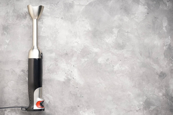 Black plastic electrical hand blender with stainless steel body on the gray background, place for text. Top view. - Photo, Image