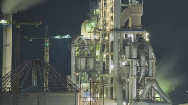 Timelapse van verlichte cementfabriek met hoge fabrieksstructuur en torenkranen op industrieterrein 's nachts. Fabricage en mondiaal industrieconcept - Video