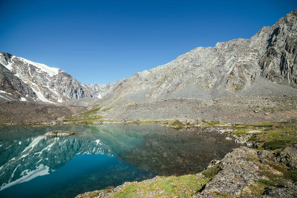 雪の山氷河湖の澄んだ水に反映されます。澄んだ空の下で山の湖の水面に氷河の反射と美しい晴れた風景。山の湖に映る岩の上の雪. - 写真・画像