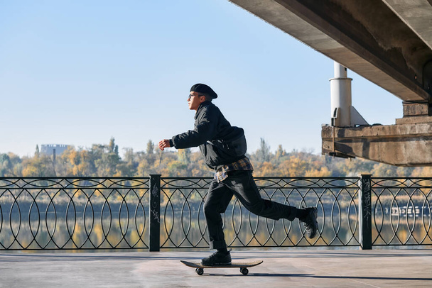 Skater rides on skateboard at empty concrete embankment on the urban background - Photo, Image
