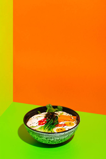 Ramen asian noodle in broth with Beef tongue meat, mushroom and pickled egg in bowl on green and orange background - 写真・画像