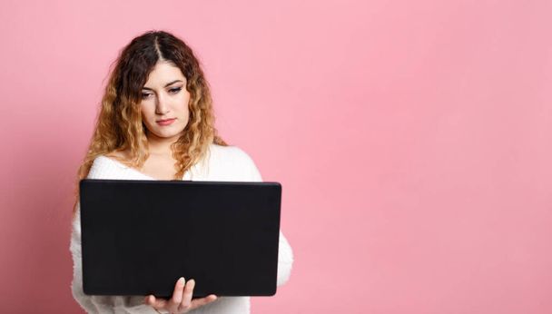 A cheerful young woman standing isolated on a pink background using a laptop computer. With a place for a copy space. - Fotografie, Obrázek