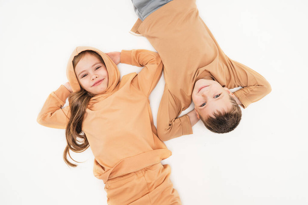 Children in sportswear lie on the floor and look into the frame. Friendship of a boy and a girl since childhood. The brother and sister put their hands behind their heads and rested. - Photo, Image