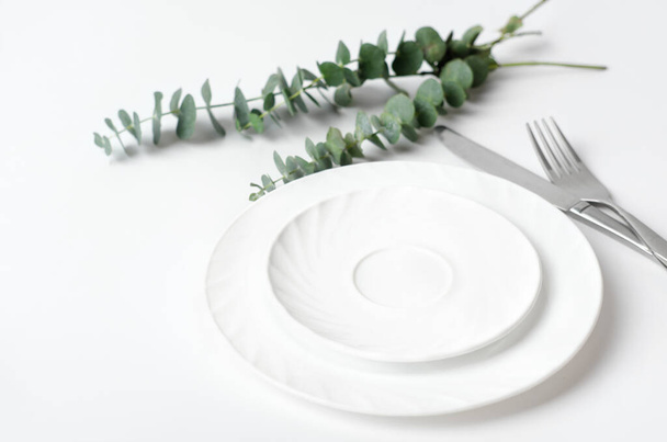 Table élégante printanière, concept de menu restaurant rustique. vaisselle blanche et argenterie à côté des branches d'eucaliptus sur une table. maquette pour le placement de repas.  - Photo, image