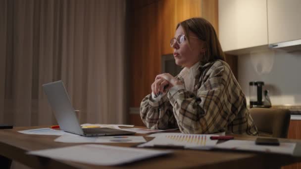 Een gefocuste vrouw met een bril, werkend aan financiële documenten, zittend op de werkplek met een laptop app, kijkt gefocust, maakt een taak af, bereidt een rapport voor, controleert een rapport. - Video