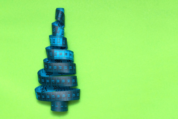 Christmas tree made of measuring tape on a green background. The concept of dieting during the Christmas holidays, weight loss, proper nutrition, overeating. Weight gain in the New Year. copy space - Foto, afbeelding