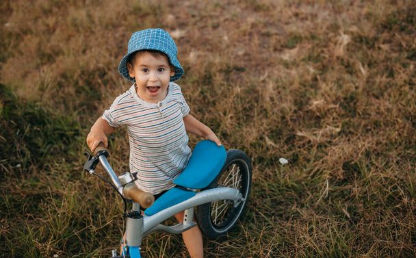 Első látásra egy kis kaukázusi fiú kezében egy biciklivel. Mosolyog a kamera előtt. Egészséges életmód. Családi hétvége. Felülnézet. - Fotó, kép