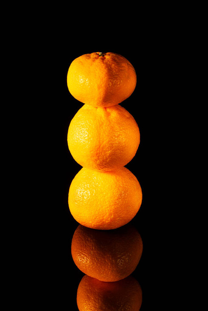 pyramid of fresh tangerines on a black table with reflection, close-up - Foto, Bild