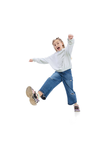 Dynamic portrait of little girl, kid in casual clothes jumping, having fun isolated on gray studio background. - Fotografie, Obrázek