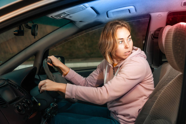 右利きの車を運転怖がって若い白人女性の肖像画、バック警察のサイレンの光を見て。交通事故や追跡の概念. - 写真・画像