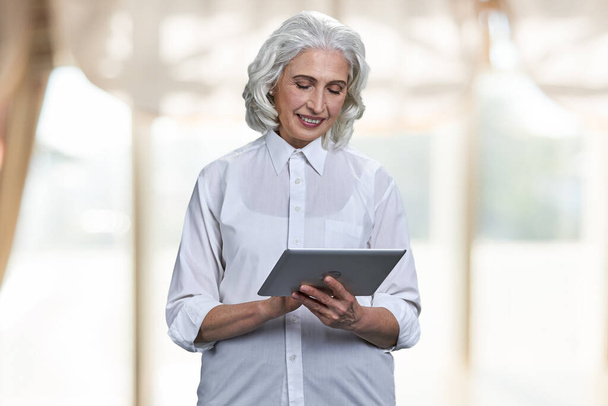 Елегантна старша жінка тримає цифровий планшет на розмитому фоні
. - Фото, зображення
