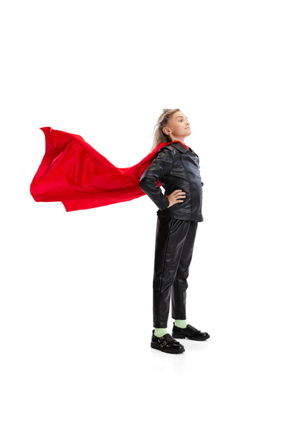 One cute little girl wearing red cape and black costume standing isolated on gray studio background - Foto, Imagen