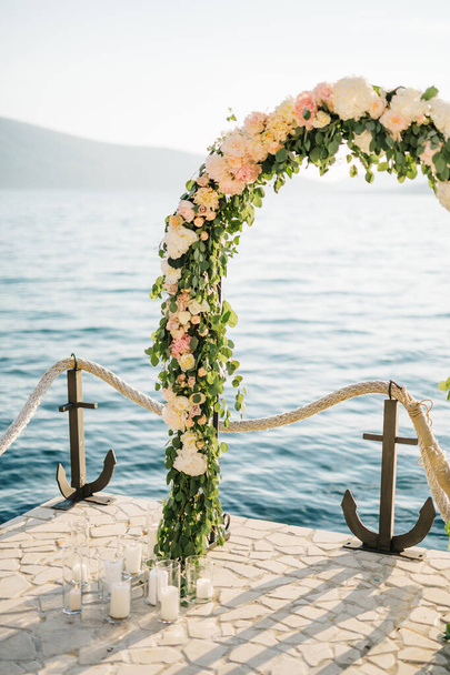 Hochzeitsbogen steht auf einem gepflasterten Steg an einem Seilzaun mit Ankern - Foto, Bild