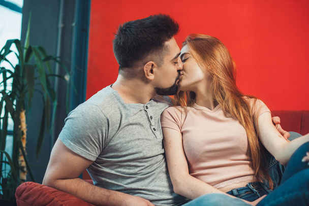 Homme et femme caucasiens s'embrassent, se câlinent pendant qu'ils sont assis sur le canapé. Passer le week-end ensemble à la maison. Temps en famille. - Photo, image