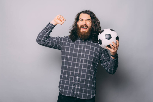 Mutlu sakallı adam elinde futbol topu tutuyor ve en sevdiği takım zaferini kutluyor. - Fotoğraf, Görsel