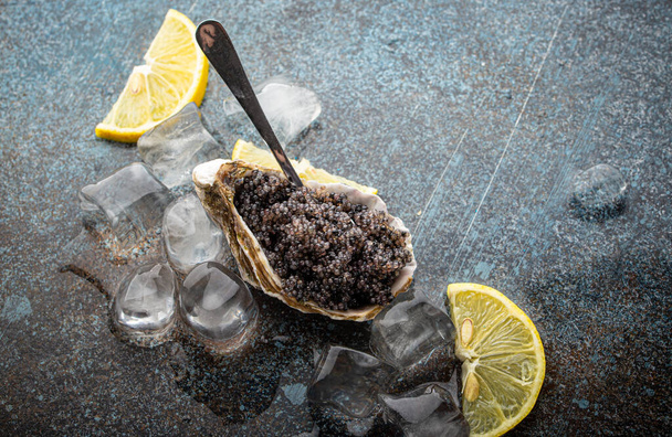 Caviale nero servito in guscio di ostrica con cucchiaio con spicchi di limone e cubetti di ghiaccio - Foto, immagini