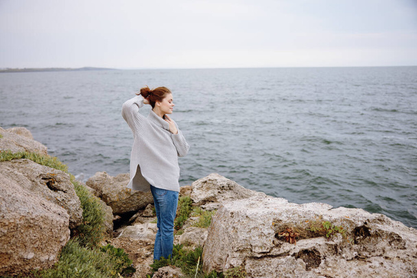 灰色のセーターを着たきれいな女性が岩だらけの海岸の自然生活をしています - 写真・画像