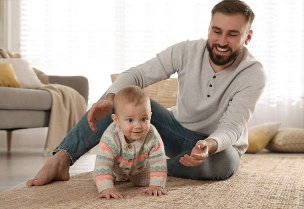 Happy young father helping his cute baby to crawl on floor at home - Photo, Image
