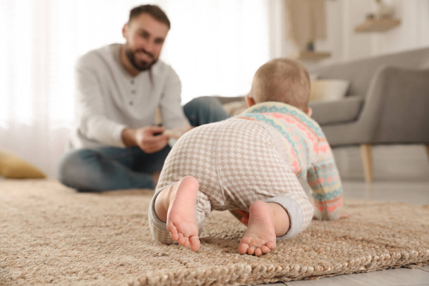 Happy young father watching his cute baby crawl on floor at home - Foto, afbeelding