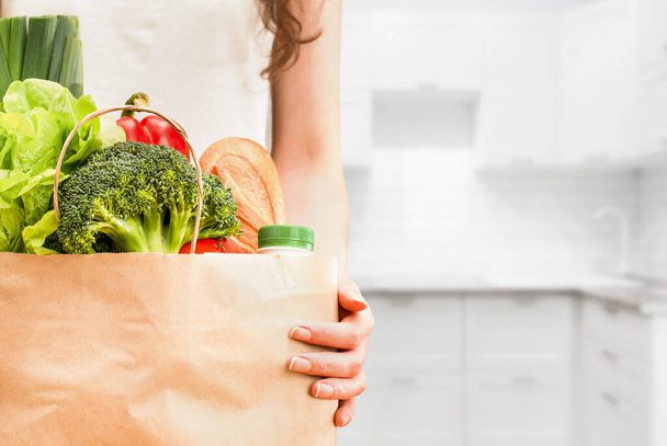 manos femeninas con bolsa de papel de comestibles sobre fondo de cocina - Foto, imagen