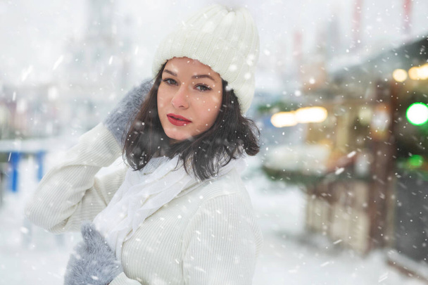 Encantadora joven lleva sombrero blanco caminando en el parque de invierno durante las nevadas. Espacio vacío - Foto, imagen