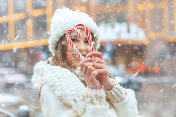 Mujer rubia alegre sosteniendo dulces en la feria de invierno de vacaciones durante las nevadas. Espacio para texto - Foto, imagen