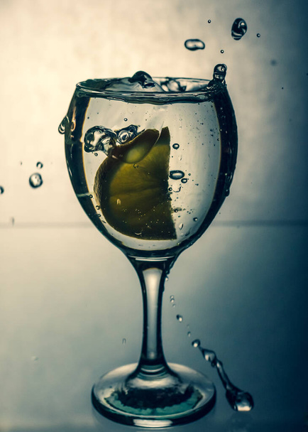La rodaja de limón salpica en un vaso de agua, aislada sobre un fondo degradado. - Foto, Imagen