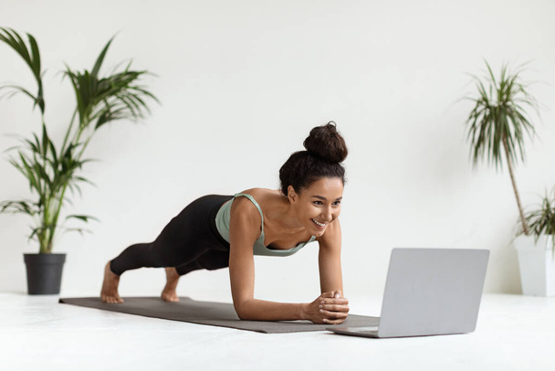 Huiselijke trainingen. Sportieve jonge vrouw doet Plank Oefening in de voorkant van laptop - Foto, afbeelding