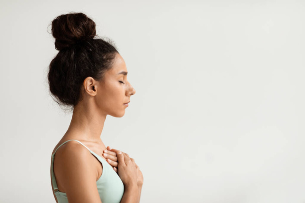 Profile of calm young woman with hands on chest and closed eyes - Photo, Image