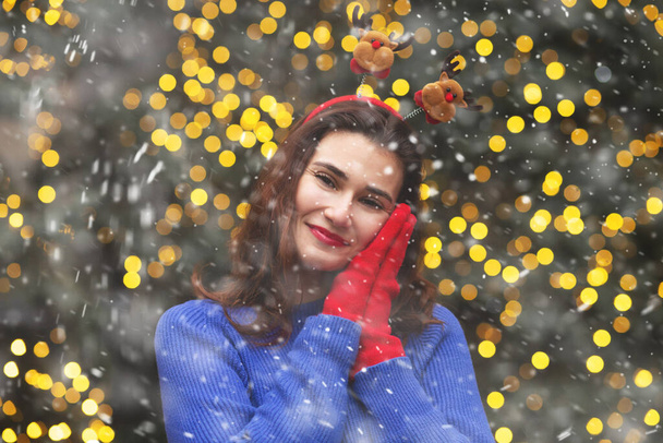 Krásná brunetka žena nosí legrační obruč s vlasy baví na vánočním stromě během sněžení. Prázdné místo - Fotografie, Obrázek