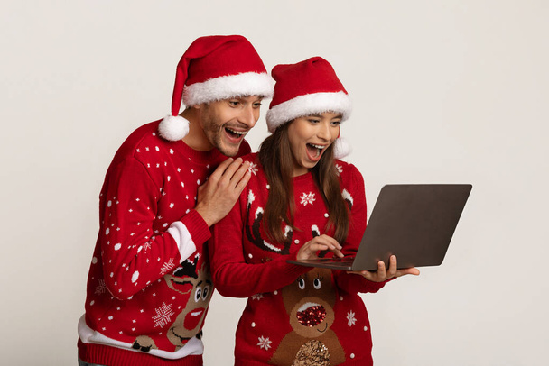 Online Wygraj. Szczęśliwa para podekscytowany w Santa kapelusze patrząc na ekranie laptopa - Zdjęcie, obraz
