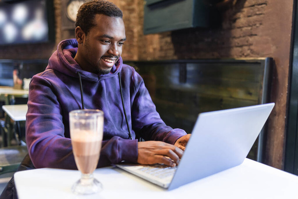 Усміхнений чорний чоловік друкує на ноутбуці під час віддаленої роботи
 - Фото, зображення