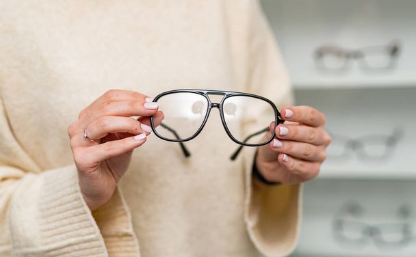 Fashionable eyeglasses lens holding in hands. Eyeglasses in woman hands. - Foto, imagen
