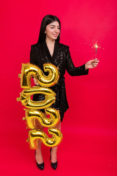 A young woman in a shiny dress and high-heeled shoes holds the numbers 2022 and a sparkler - Foto, afbeelding