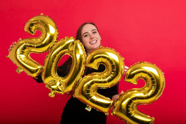 A happy brunette in a black dress holds the numbers 2022 on a red background - Zdjęcie, obraz