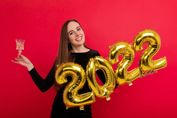 Holidays, New Year's Eve - a young woman in a black dress holding a glass of champagne and the numbers 2022 - Foto, afbeelding