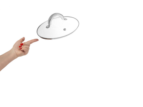 Woman's hand with red nails points to transparent glass pot or frying pan lid with a metal handle flying levitating in air.Isolated on white background,copy space.Concept of hot utensil in kitchen. - Photo, Image