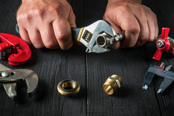 Professionelle Klempner verbindet Messing Armaturen mit einem verstellbaren Schraubenschlüssel. Nahaufnahme der Hand des Meisters bei der Arbeit in der Werkstatt - Foto, Bild