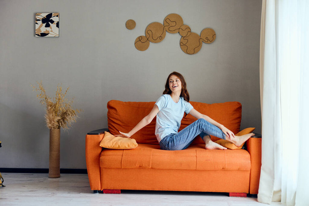 hermosa mujer en el sofá naranja en la sala de descanso posando inalterada - Foto, Imagen
