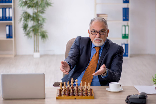 Old businessman playing chess at workplace - Foto, imagen
