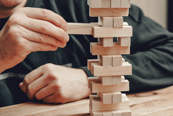 The hands of a man playing a board game builds a tower from wooden blocks. - Φωτογραφία, εικόνα