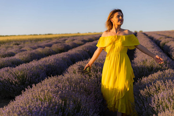 Bella e bella giovane donna in abito giallo si rilassa e gode di una passeggiata nel campo di lavanda al tramonto, tonica - Foto, immagini