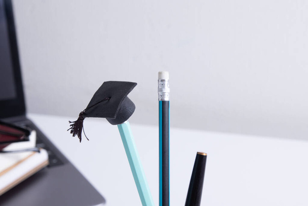Een pet op een potlood op de achtergrond van een bureaublad met kantoorbenodigdheden. Online home learning concept - Foto, afbeelding