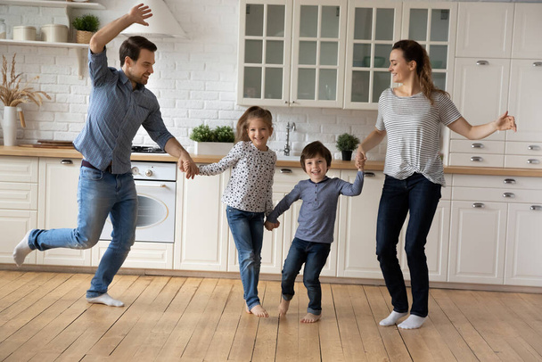 Glückliche Familie mit zwei Kindern tanzt in moderner Küche zusammen - Foto, Bild